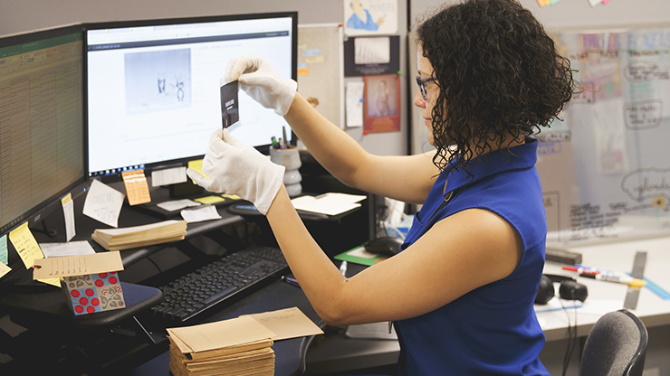 An archivist wearing gloves and examining a photographic negative