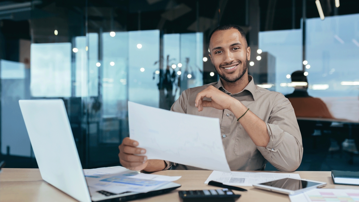 A smiling businessman holding a document at his desk in a modern office