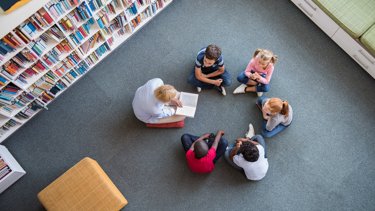 A teacher reading to a group of children sitting in a circle in a library