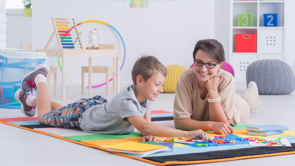 A smiling teacher and young boy engaging in a learning activity with blocks 