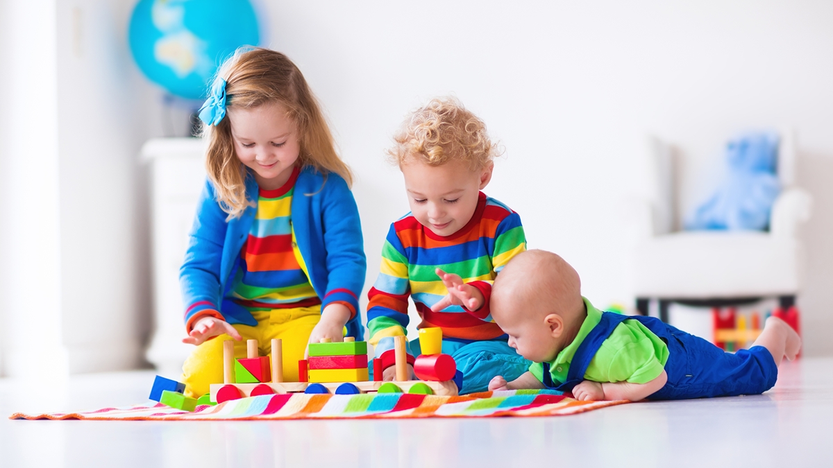 Three young children in colorful outfits playing with wooden blocks 