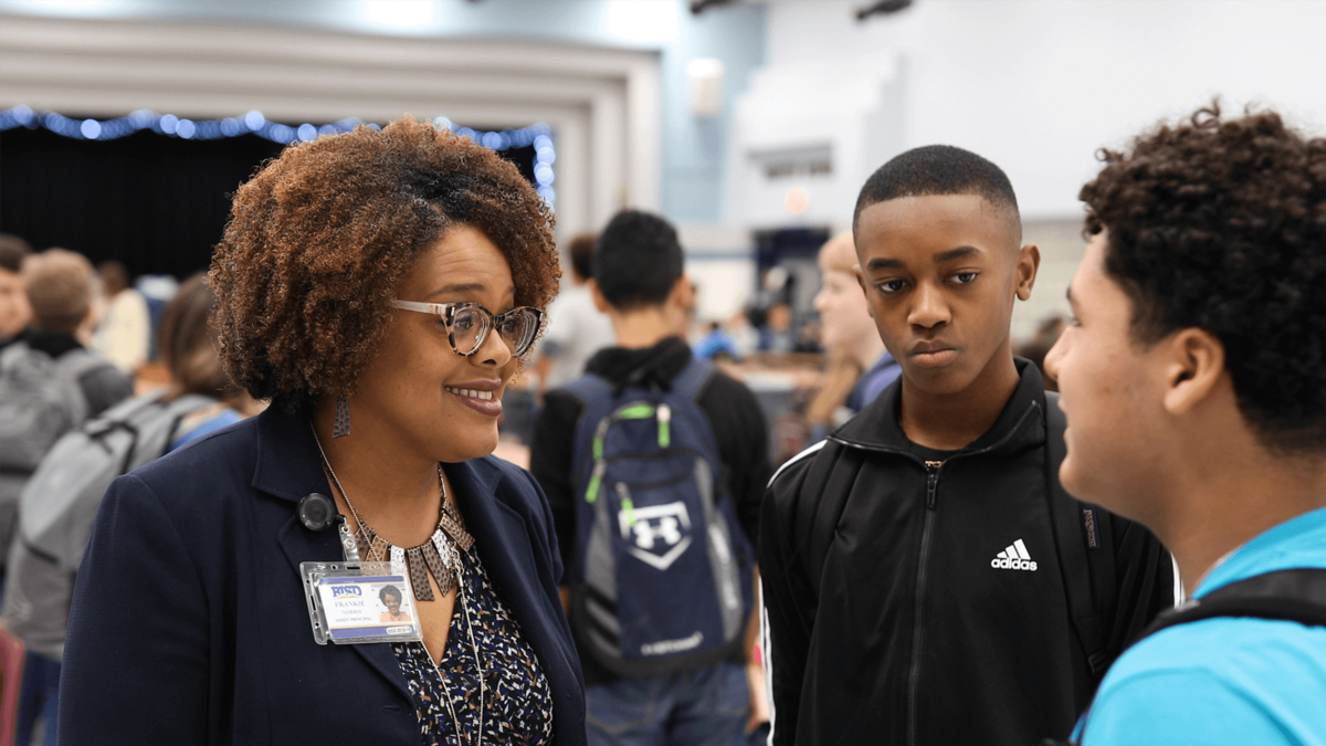 A school administrator talks with two attentive high school students