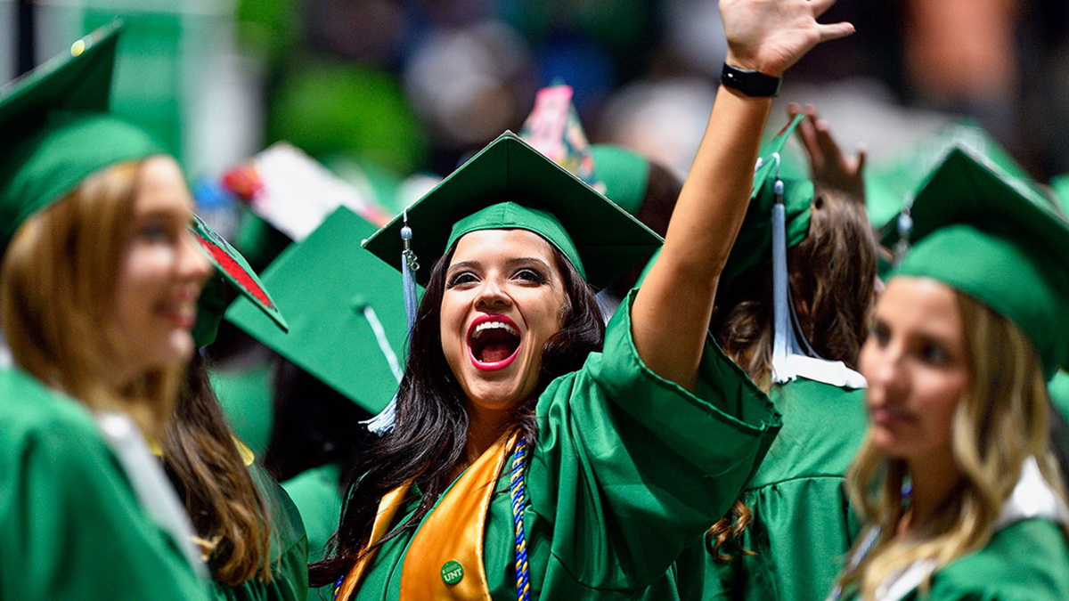 A graduate in a green cap and gown celebrating 