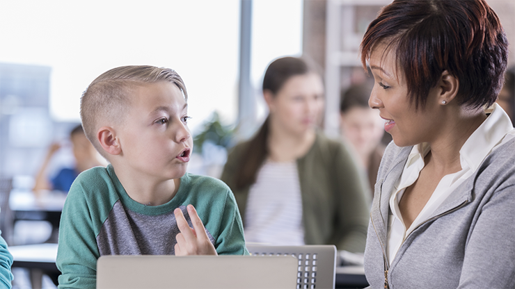 A young boy talking with a teacher in a classroom