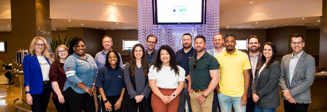 A group of professionals posing for a group photo in a modern lobby area. A screen in the background displays logos and text, while the environment features contemporary decor.