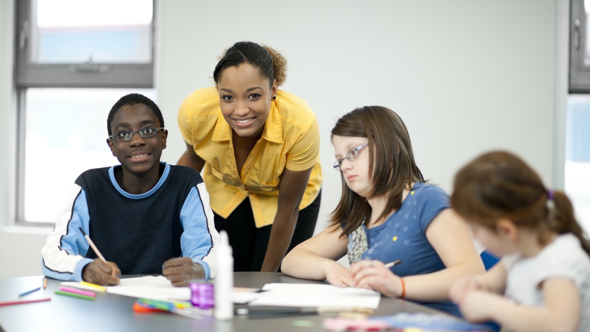 A smiling teacher guiding students with diverse abilities