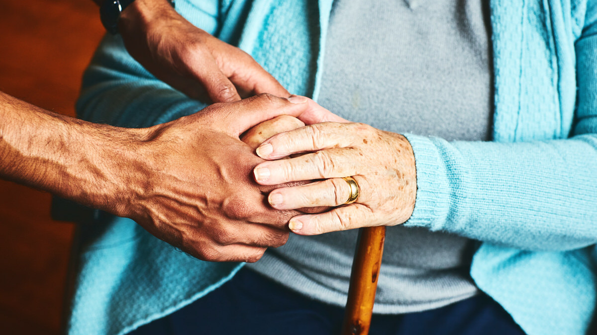 A close-up of hands supporting an elderly individual 