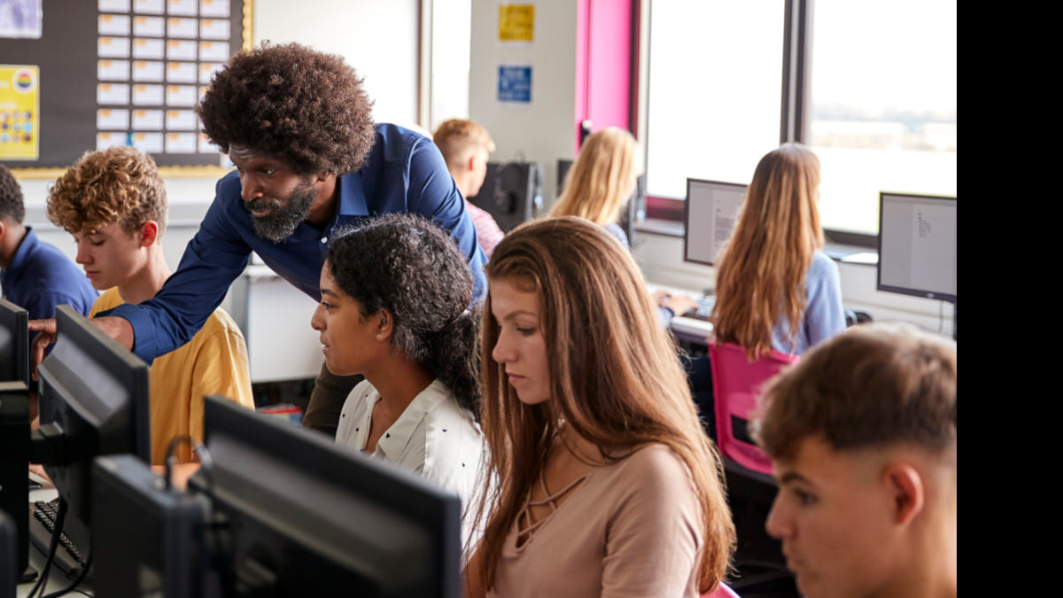 A teacher assisting high school students in a computer lab 