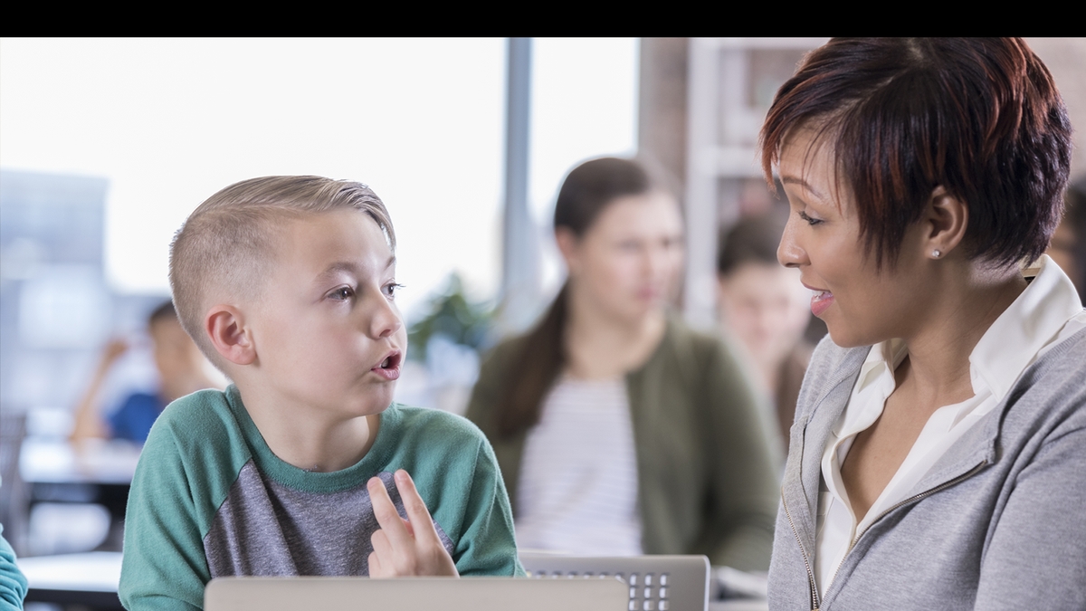 A young boy talking with a teacher in a classroom