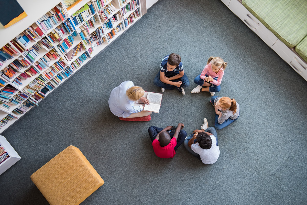 A teacher reading to a group of children sitting in a circle in a library