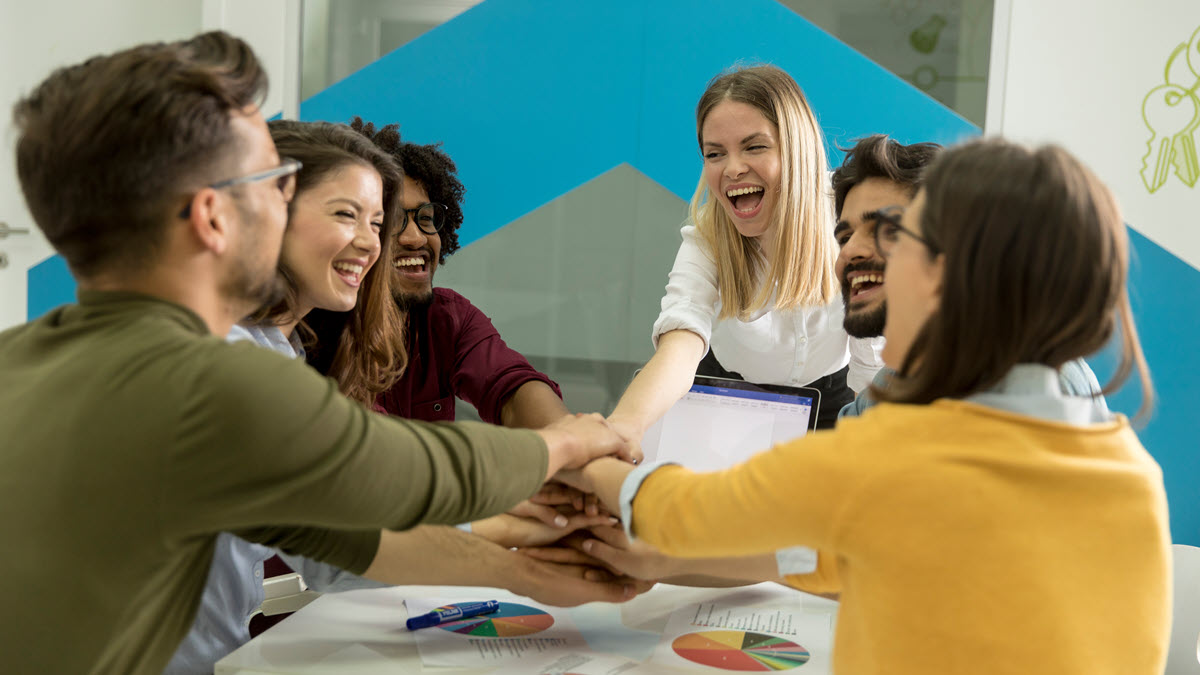 A team of people stacking hands together over table engaged in teambuilding 