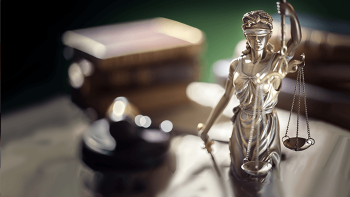 Statue of lady of justice holding even scales and sword on desk with a gavel
