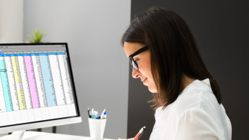 female in lab coat reviewing spreadsheets of data on computer screen