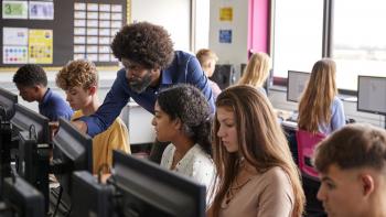 Male teacher helping teenage female high school student working in computer class.
